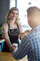 Waitress serving a cup of coffee and croissant to customer