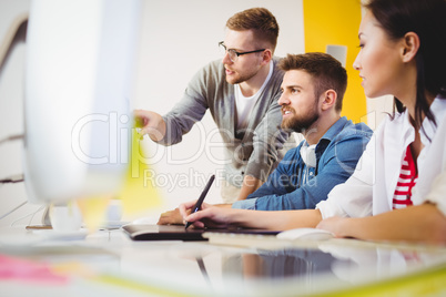 Executive pointing at computer monitor to colleagues in creative office
