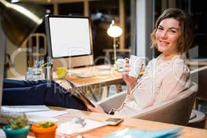 Businesswoman holding digital tablet and coffee cup at her desk