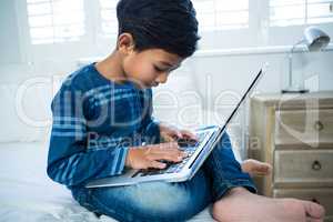 Boy using laptop while relaxing on bed