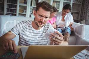 Worried man calculating bills while his wife and daughter sitting on sofa