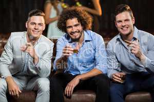 Three happy friends having cigar and whisky in bar