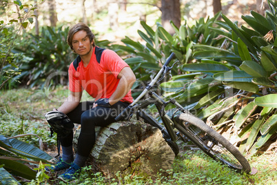 Portrait of exhausted male mountain biker relaxing on a tree trunk in the forest