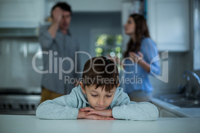 Upset boy sitting while couple having argument in background