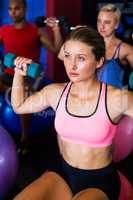 Thoughtful young woman lifting dumbbell in gym