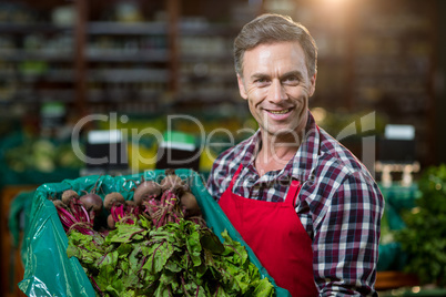 Smiling male staff holding a crate of fresh vegetables at supermarketÃ?Â 