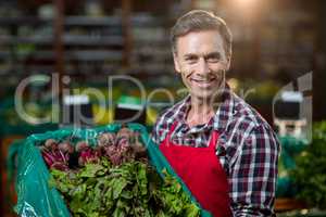 Smiling male staff holding a crate of fresh vegetables at supermarketÃ?Â 