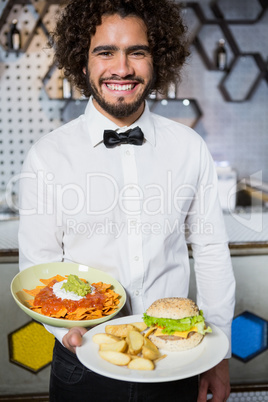 Waiter holding plates of snacks and burger in bar