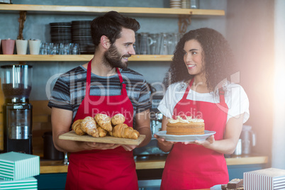 Waiter and waitress holding a tray of croissants and cake