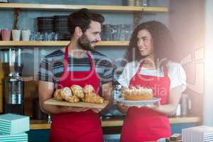 Waiter and waitress holding a tray of croissants and cake