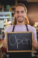 Portrait of smiling waiter holding chalkboard with open sign