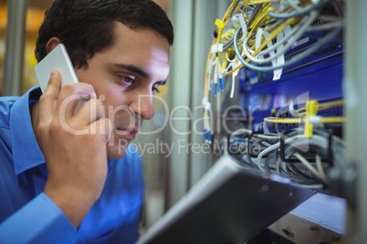 Technician talking on mobile phone while analyzing server