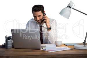 Businessman talking on mobile phone while working on laptop