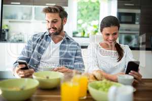 Couple using mobile phone while having breakfast