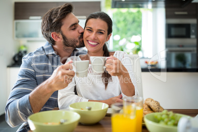 Man kissing on woman cheeks while having breakfast