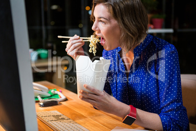 Businesswoman eating noodles at her desk