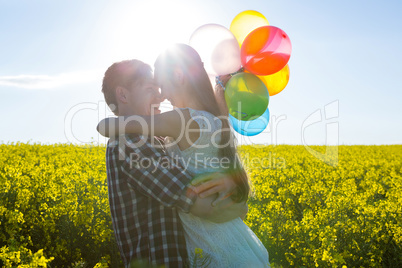 Couple holding colorful balloons and embracing each other in mustard field