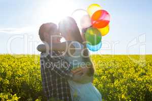 Couple holding colorful balloons and embracing each other in mustard field