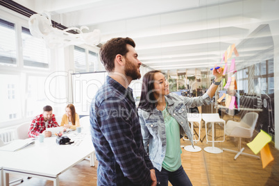 Smiling business people looking at multi colored sticky notes on glass