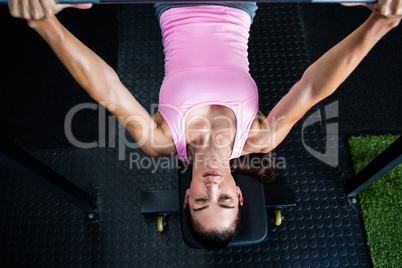 Woman holding barbell while lying on bench press in gym