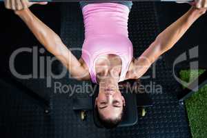 Woman holding barbell while lying on bench press in gym
