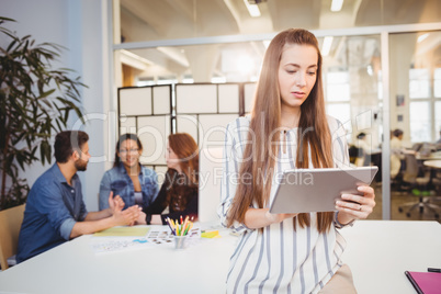 Businesswoman using digital tablet against coworkers