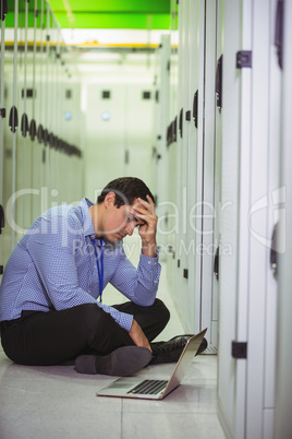 Stressed technician sitting on floor and looking at laptop