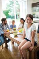 Portrait of girl sitting on dining table while family having breakfast in background