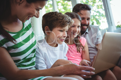 Parents sitting on sofa with their children and using laptop in living room