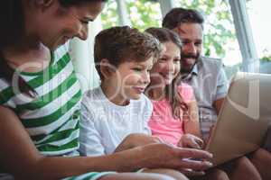 Parents sitting on sofa with their children and using laptop in living room