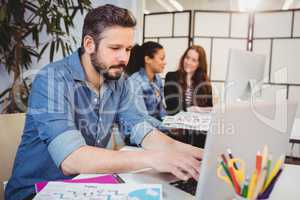 Businessman using laptop at desk against female coworkers