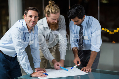 Businessman smiling at camera while colleagues discussing over blueprint