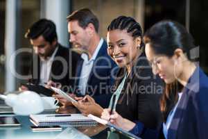 Businesswoman using digital tablet while colleagues writing notes