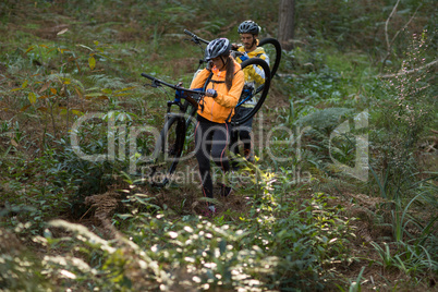 Biker couple carrying their mountain bike and walking in forest