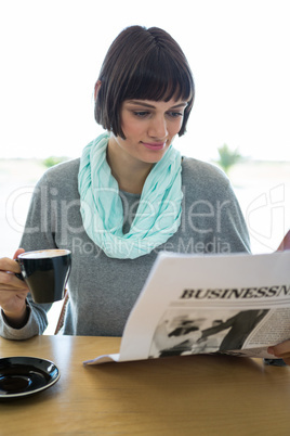 Woman reading newspaper while having coffee