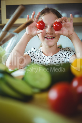 Playful girl holding cherry tomato on her eye