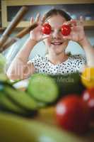 Playful girl holding cherry tomato on her eye