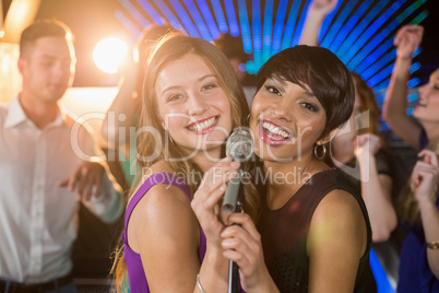Two beautiful women singing song together in bar