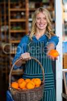 Smiling female staff holding basket of fruit in organic section