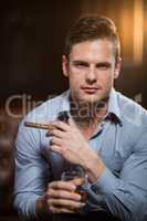 Man holding a cigar and glass of whisky in bar