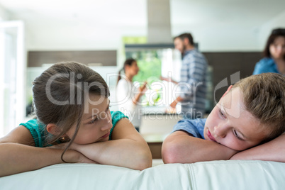 Sad kids leaning on sofa while parents arguing in background