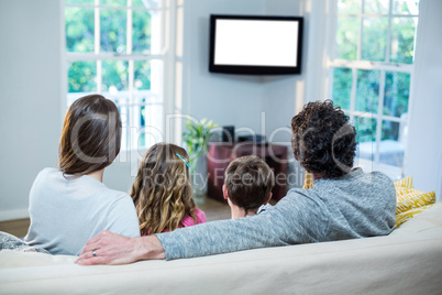 Family watching television while sitting on sofa