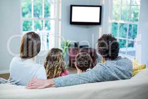 Family watching television while sitting on sofa