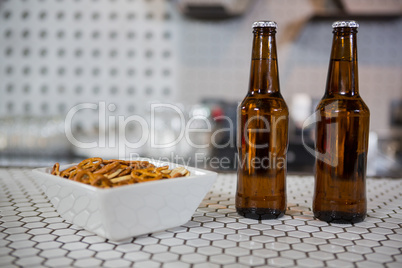 Beer bottles and bowl of snacks on bar counter