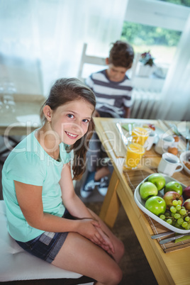 Portrait of girl sitting on dining table while boy in background