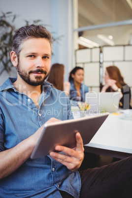 smiling businessman using digital tablet against female coworkers