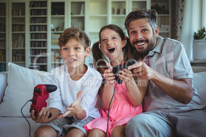 Father sitting on sofa with his children and playing video games