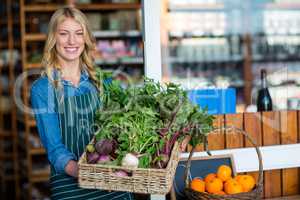 Smiling staff holding a basket of fresh vegetables in organic section