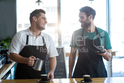 Smiling waiter interacting while making cup of coffee at counter