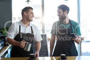 Smiling waiter interacting while making cup of coffee at counter